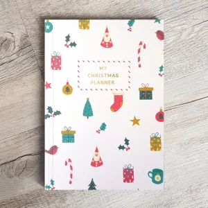 Christmas planner laid flat on a surface showing the front cover. The cover has Christmas trees, stockings, candy canes, candles