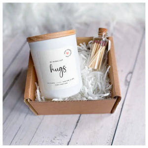 no words just hugs scented candle gift set shown here with the candle laid in the gift box and the glass matches jar laid next to it.