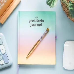 Gratitude journal with vibrant multicoloured cover laid flat with a pen sat on top